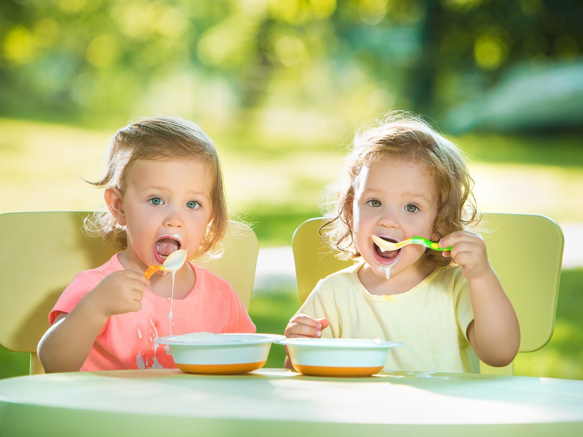 Two happy toddlers enjoying a meal together outdoors